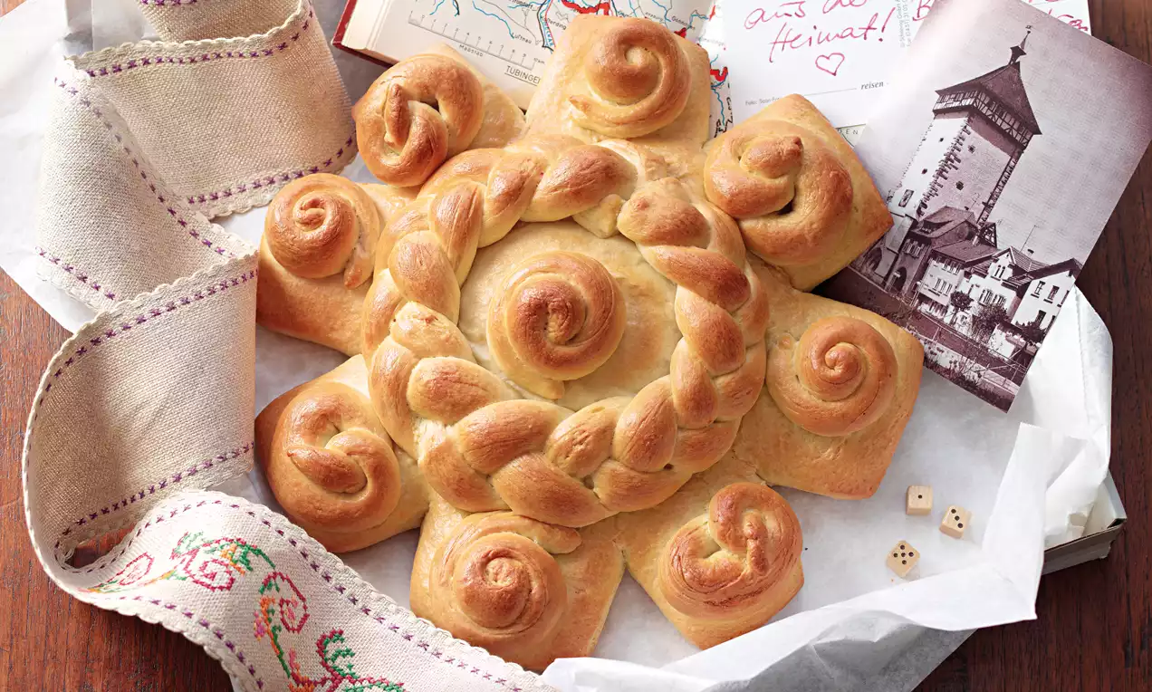 Goldbraune, sternförmige Reutlinger Mutschel mit geflochtenem Mittelstück und geschwungenen Hörnchen auf Stofftuch neben Postkarten