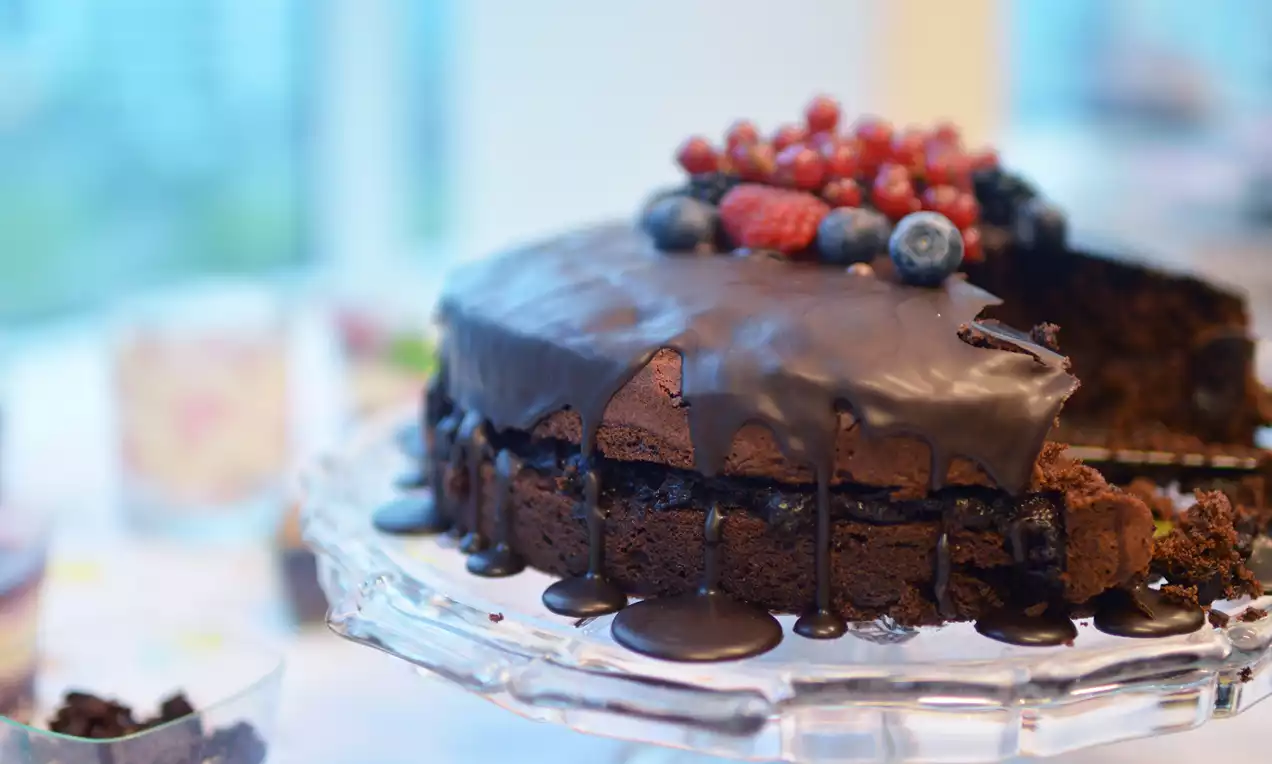 Gâteau au chocolat foncé avec glaçage coulant, baies rouges et myrtilles en garniture sur un plat en verre transparent