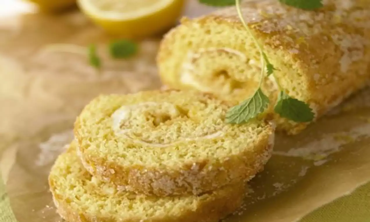 Sitronrullekake med gyllen overflate og sukret tekstur, fylt med lys krem og pyntet med sitronmelisse på bakepapir