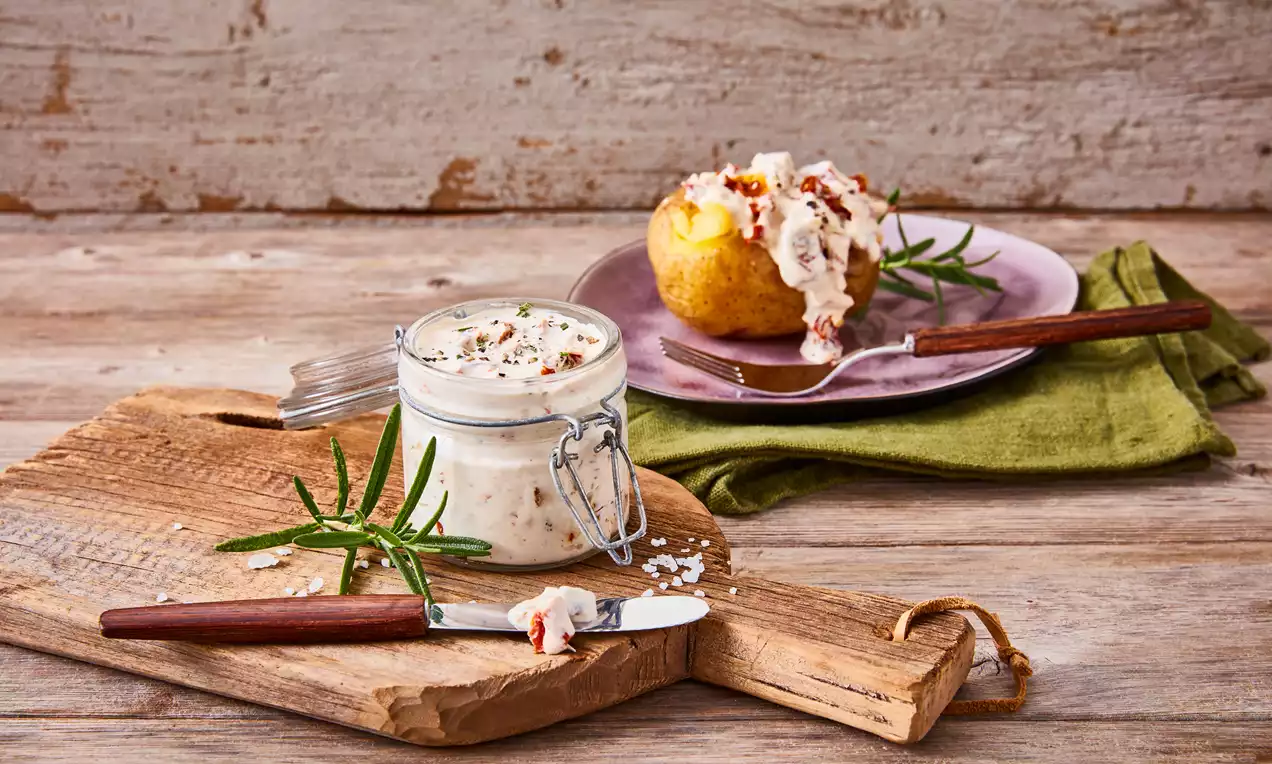 Cremiger Tomaten-Rosmarin-Dip in einem Bügelglas auf einem rustikalen Holzbrett, dekoriert mit frischem Rosmarin und Besteck