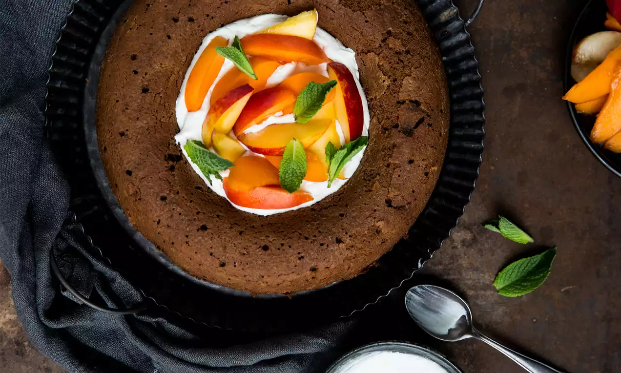 Savarin moelleux brun café entourant une crème blanche garnie de tranches de fruits orangés et jaunes avec feuilles de menthe