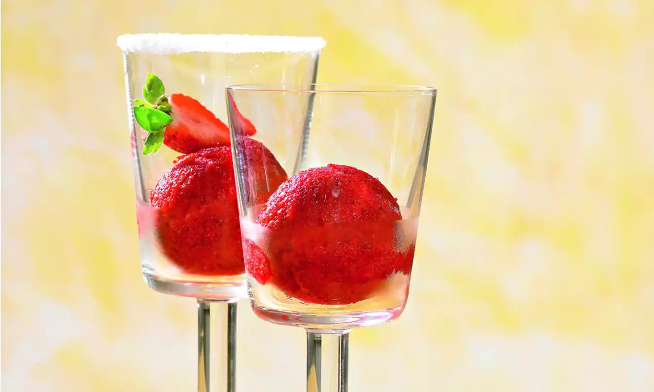 Bile de sorbet din căpșuni roșii intens, cu textură fină, așezate în pahare transparente decorate cu frunze de mentă și felii de căpșuni