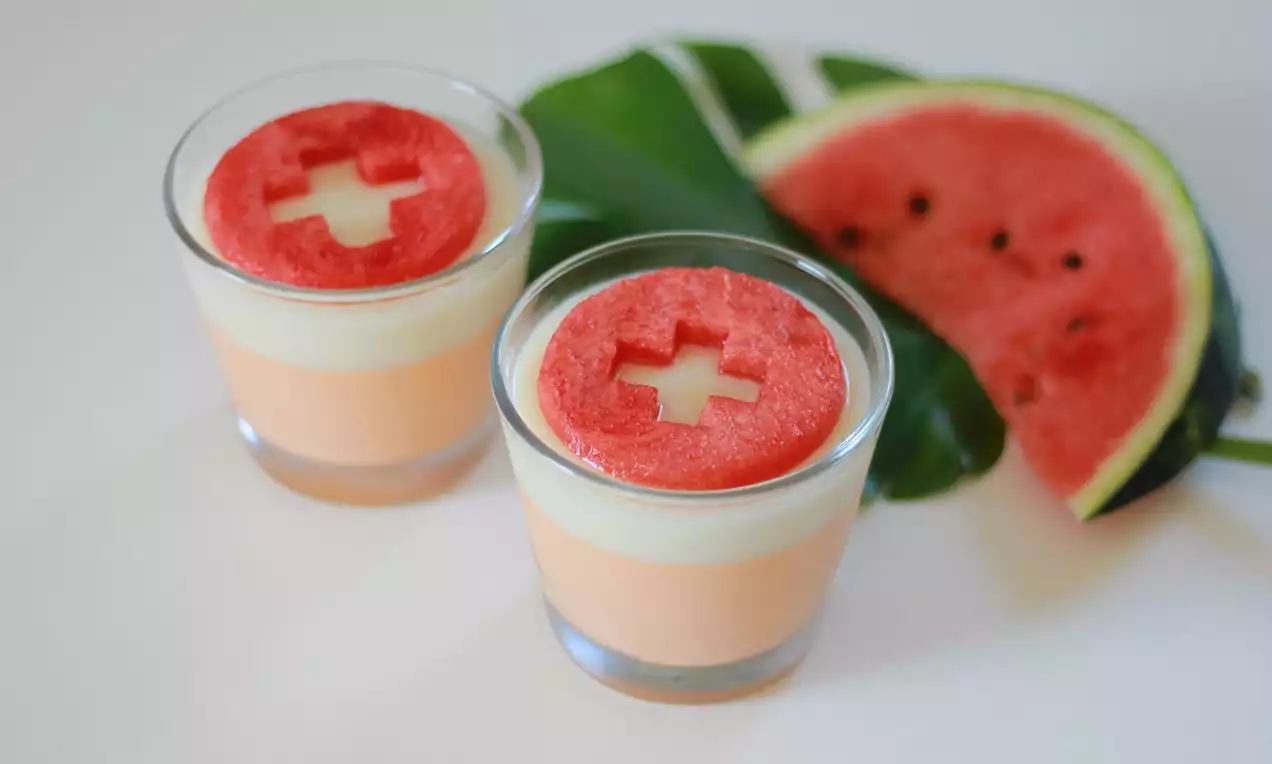 Panna cotta en verre aux couches pêche et blanche, surmontée de rondelles de pastèque rouge vif sur une feuille verte