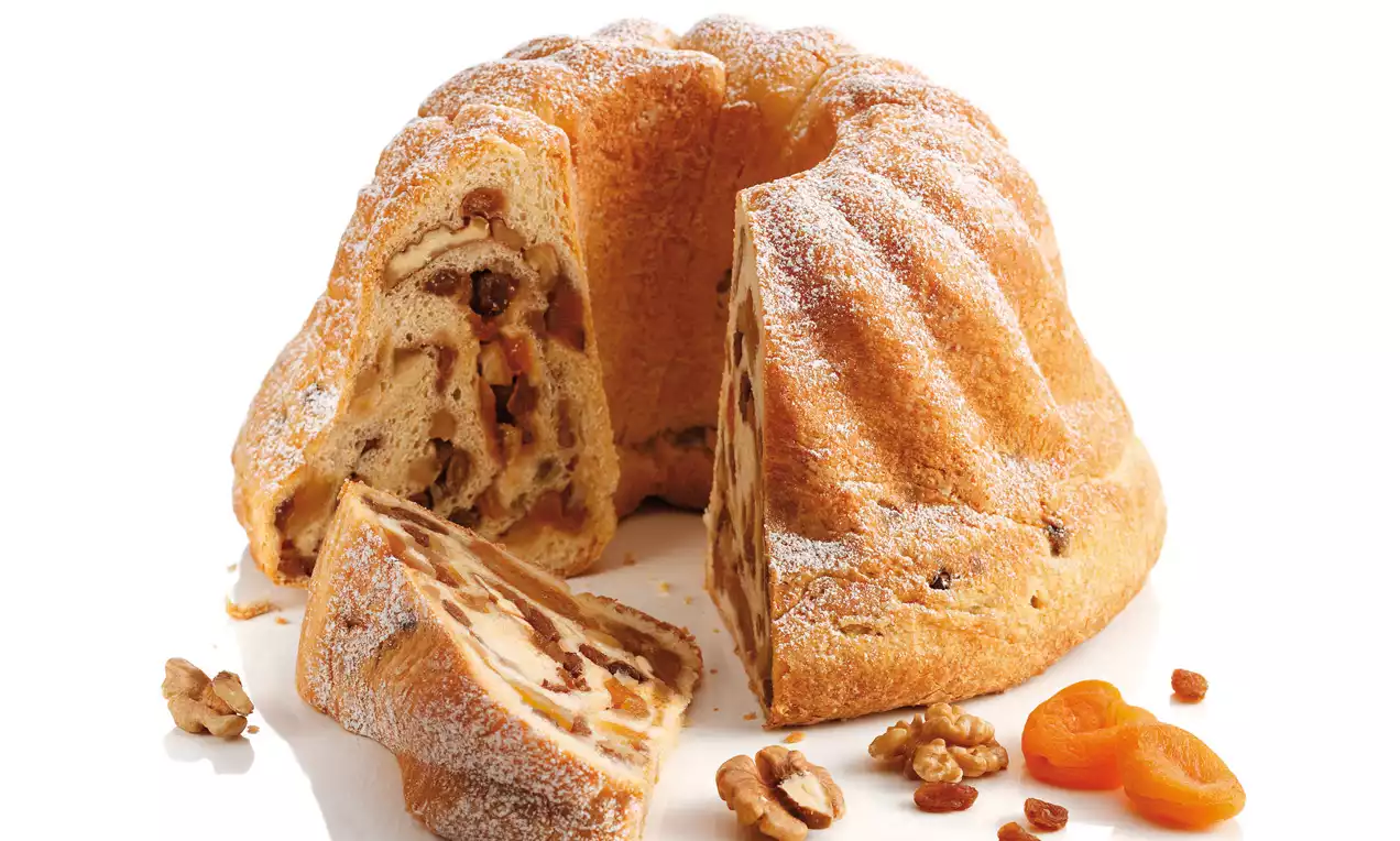 Goldbraun gebackener Gugelhupf mit welliger Oberfläche, Staubzucker, angeschnitten, gefüllt mit Nüssen, Rosinen und Trockenfrüchten