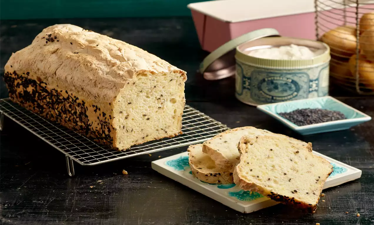 Kastiger Laib hellbraunes Kartoffelbrot mit goldener Kruste, daneben Scheiben auf gemustertem Teller, umgeben von Schälchen und Dekorelementen