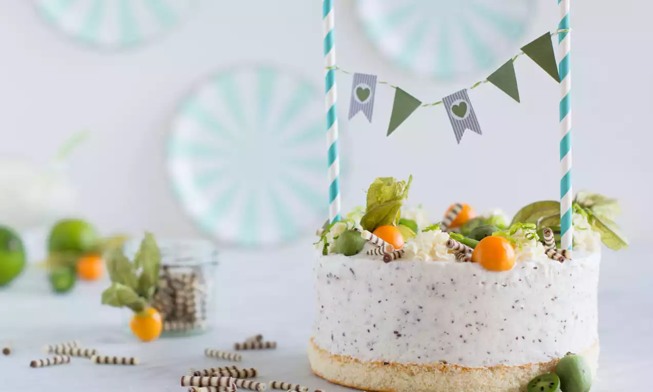 Stracciatella-Biskuit-Eistorte mit weißer, gesprenkelter Creme, luftigem Biskuitboden, Physalis und Schokoröllchen, dekoriert mit grünem Wimpelbanner