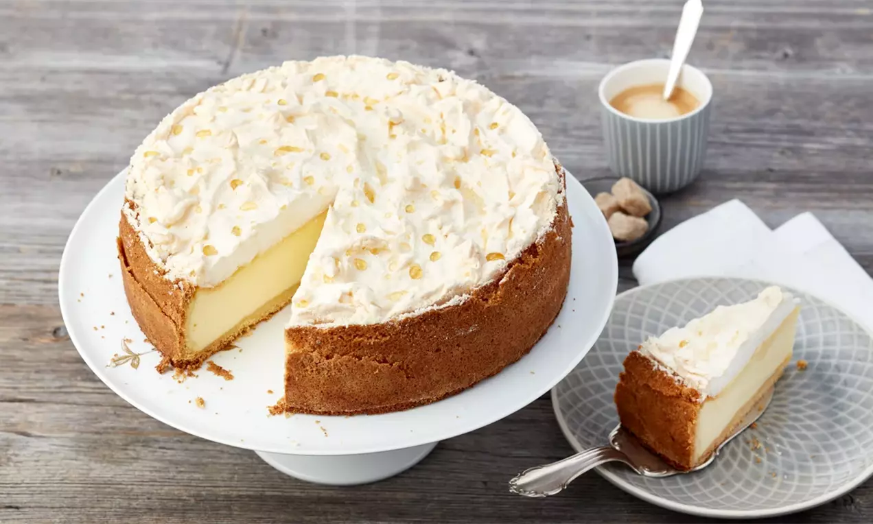 Чийзкейк с пухкав слой бяла сметана, златисто-кафява основа и кремообразен жълт център върху бяла поставка до чаша кафе