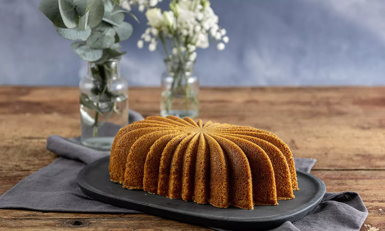 Златистокафява торта с крем Парадис във форма на извити листа с равномерна текстура върху тъмна плочка, заобиколена от свежи цветя