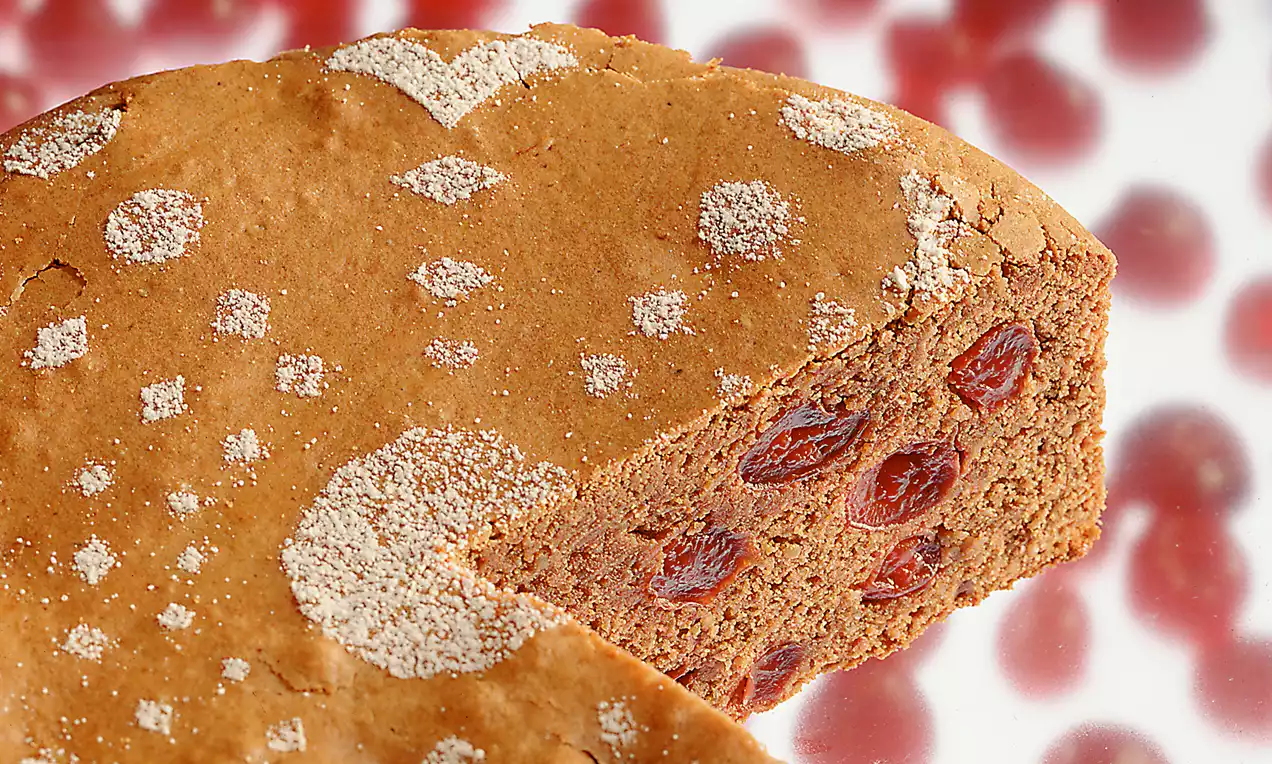 Prager Kirschtorte mit brauner Oberfläche, Puderzucker-Muster und saftigen roten Kirschen im Anschnitt auf hellem Hintergrund